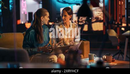 Portrait of Two Female Creative Colleagues Collaborating and Pointing at the Laptop Screen in Office Hub. Lead Designer Discussing Work with Assistant and Choosing Marketing Strategy Stock Photo