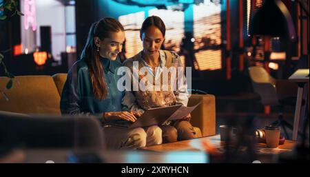 Two White Females Having a Discussion in Meeting Room Behind Glass Walls in an Agency. Creative Director and Project Manager Compare Business Results and App Designs on Laptop in an Office Stock Photo