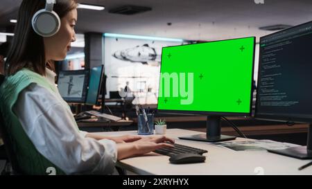 Female Asian Game Programmer Coding On Desktop Computer With Green Screen Chromakey On Display In Game Development Studio Office. Focused Woman Does Gameplay Engineering For New 3D RPG Video Game. Stock Photo