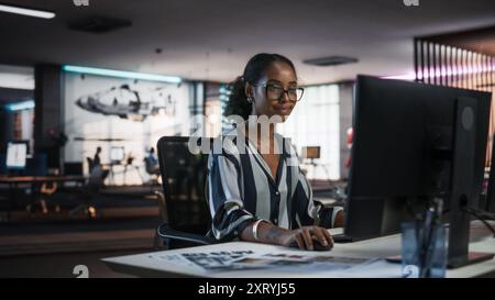 Young Black Woman Working on Desktop Computer in Creative Office. Multiethnic Marketing Manager Writing Email Messages, Developing Social Media Strategy, and Researching Project Plan Details Online Stock Photo