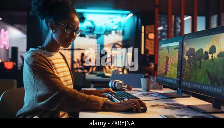 Portrait of Female Video Game Designer Working on a New 3D Level on Desktop Computer in Creative Office. Black Focused Woman Creating Metaverse and Adding Details to a Game Environment Stock Photo
