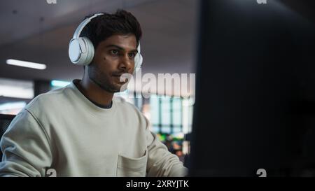 Portrait of a Stylish Indian Man Working on Desktop Computer in a Company Office. Young Male Manager Browsing Internet, Shopping Online, and Reading Social Media Posts from Friends and Colleagues Stock Photo