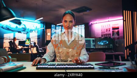 Portrait of a Female Software Developer Writing Code in a Creative Office with Neon Lights. Young Woman Focused on Typing on Keyboard and Working on Desktop Computer. Point of View of Screen Monitor Stock Photo