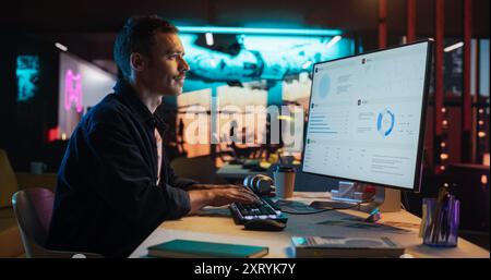 Portrait of Professional Male Developer Using Desktop Computer and Typing in Creative Office. Caucasian Man Analysing Data and Budget for the Lunch of a New Product in Big Gaming Company Stock Photo