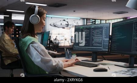 Female Asian Game Programmer Coding On Desktop Computer In Game Development Studio Diverse Office. Focused Woman Writes Lines Of Code, Does Gameplay Engineering For New Immersive 3D RPG Video Game. Stock Photo