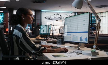 African Female Manager Using Desktop Computer With Analytics Software wth Financial Reports. Woman Working In Game Development Company Diverse Office Stock Photo