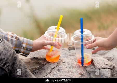 Two children drink bubble tea from plastic cups on a walk in the evening, close-up Stock Photo