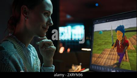 Portrait of Female Video Game Designer Working on a New 3D Level on Her Desktop Computer. Focused Woman Creating Metaverse and Design Video Game Character in Creative Office at Night Stock Photo