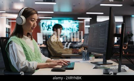 Female Asian Game Programmer Coding On Desktop Computer In Game Development Studio Diverse Office. Focused Woman Writes Lines Of Code, Does Gameplay Engineering For New Immersive 3D RPG Video Game Stock Photo