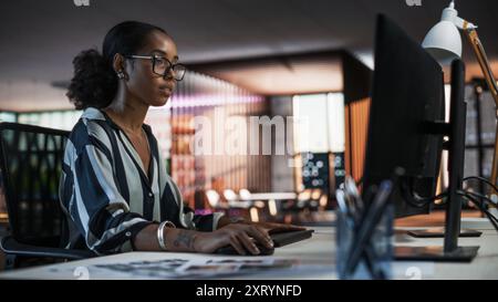 Portrait of a Beautiful Black Woman Using Desktop Computer, Analysing Data, Thinking and Solving Problems. Female Project Manager Working in Creative Agency, Reviewing Social Media Marketing Strategy Stock Photo
