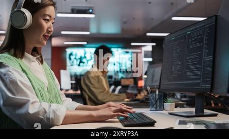 Female Asian Game Programmer Coding On Desktop Computer In Game Development Studio Diverse Office. Focused Woman Writes Lines Of Code, Does Gameplay Engineering For New Immersive 3D RPG Video Game Stock Photo