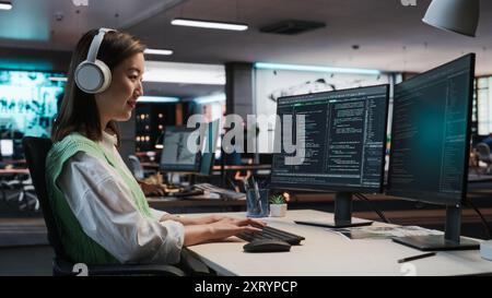 Female Asian Game Programmer Coding On Desktop Computer In Game Development Studio Diverse Office. Focused Woman Writes Lines Of Code, Does Gameplay Engineering For New Immersive 3D RPG Video Game. Stock Photo