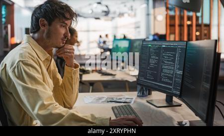 Male Caucasian Game Programmer Coding On Desktop Computer In Game Design Studio Diverse Office. Focused Man Writes Lines Of Code, Does Gameplay Engineering For New Immersive 3D Survival Video Game. Stock Photo