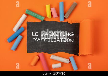AFFILIATE MARKETING. Text in French . Text under torn orange paper on a blackboard. Stock Photo