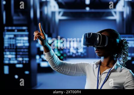 System administrator in data center uses virtual reality to prevent servers overload. Employee with VR simulation goggles in server room ensuring enough network bandwidth for smooth operations Stock Photo