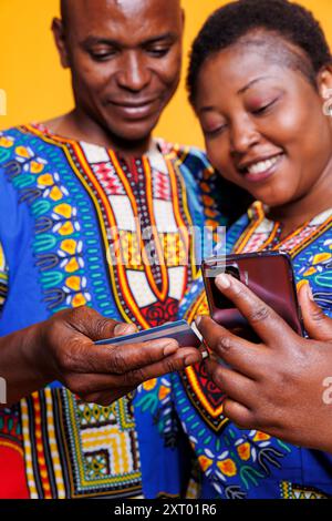 Smiling wife and husband entering credit card number on online store mobile website. Couple with cheerful expression holding smartphone and making payment while buying on internet Stock Photo