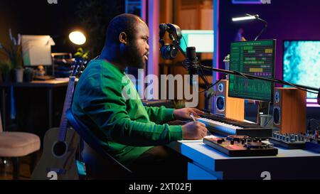 Songwriter taking notes to create new tracks for an album in his home studio, writing lyrics and harmonic elements before recording his song and editing on software, acoustical engineering. Camera A. Stock Photo