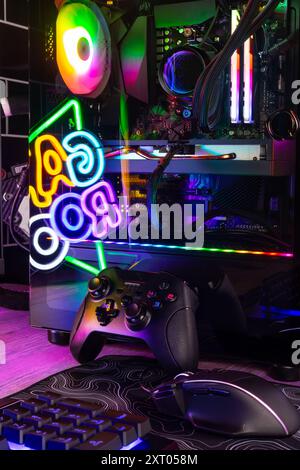 Vertical shot of colorful gaming pc desk with bright raimbow led computer gamepad mouse keyboard and steering wheel. esports video games concept  back Stock Photo