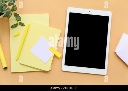 Tablet with notebooks and sticky notes on orange background Stock Photo