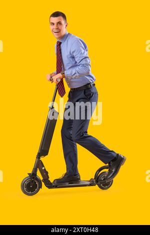 Young businessman riding electric scooter on yellow background Stock Photo