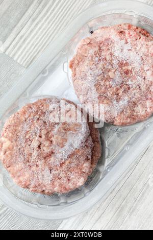 Frozen beef burgers in plastic tray packaging thawing.  On a grey wood background Stock Photo