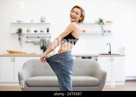 Happy woman celebrating weight loss in large jeans at home Stock Photo