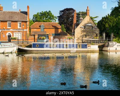 Saint Helen's Wharf is a noted beauty spot on the River Thames, just upstream of the medieval bridge at Abingdon-on-Thames. The wharf was for centuries an important transport and shipping link up the Thames and between canals from Oxford and the Midlands. Fine merchant houses rub shoulders with alms houses and the Saxon-era Saint Helens Church. Here we see pleasure and house boats moored alongside the Long Alley Alms Houses,  viewed on a fine mid-summer day from the north bank of the river. And a line of Canada Geese chooses this moment to swim past... Stock Photo