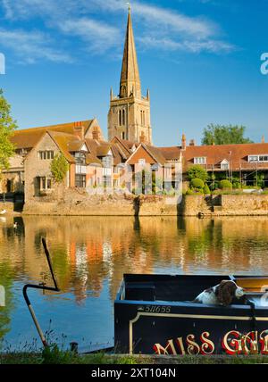 A fine view of the Thames at Abingdon, early on a summer morning. We're on the south bank of the river, looking across to the Anglo Saxon church of St Helens that the wharf is named after, past a moored houseboat  and curious spaniel in the foreground. Stock Photo