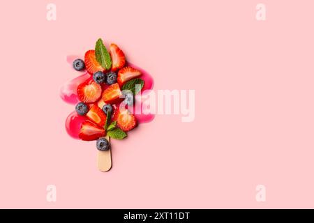 A strawberry popsicle with various colorful fruits arranged to mimic an ice cream scoop, on a pink background. Stock Photo