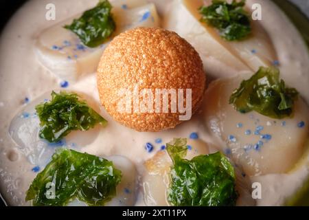 Top view of tasty homemade cream soup with sea scallop decorated with green lettuce and deep fried cheese ball and blue drops Stock Photo