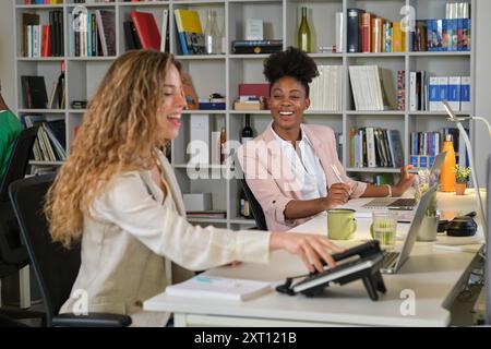 Charming diverse female coworkers sitting at table in contemporary workplace and working together Stock Photo