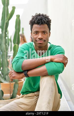 Smiling African American male in casual clothes sitting on bench on terrace and looking at camera Stock Photo