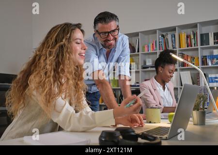 Low angle of male and female employees speaking about business strategy while using laptop and working in creative workspace with multiracial colleagu Stock Photo