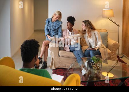 High angle of group of multiethnic colleagues sitting on couch and working on new business project together in office lounge Stock Photo