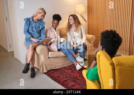 Company of multiethnic colleagues gathering on couch and talking about new business strategy while working in office lounge together Stock Photo