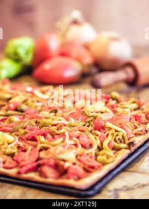 A freshly baked vegetable pizza adorned with vibrant bell peppers and onions, presented on a rustic kitchen table alongside raw ingredients including Stock Photo