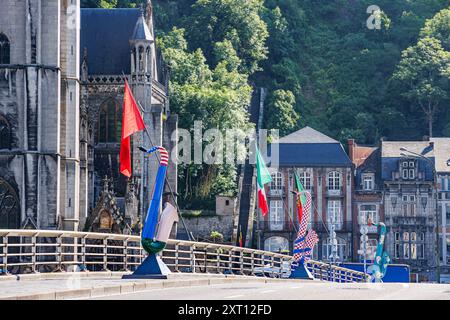 Dinant, Namur, Wallonia, Belgium. June 5, 2024. Pedestrian sidewalk over bridge, flags and saxophone sculptures in resort town of Dinant, buildings an Stock Photo