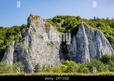 Imposing huge high rock formation against blue sky, standing out from surrounding lush green trees, sunny summer day in Namur province, Wallonia, Belg Stock Photo