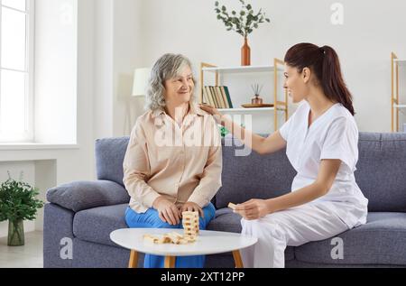 Supporting caring kind female medical nurse playing game with senior patient, assisted living  Stock Photo