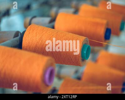 Rows of orange yarn spools mounted on machines in a textile factory, illustrating the thread production process Stock Photo