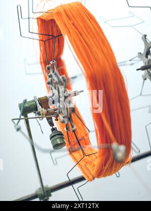 A close-up of vibrant orange yarn being processed in an industrial textile machine at a factory, with a blurred background emphasizing the machinery Stock Photo