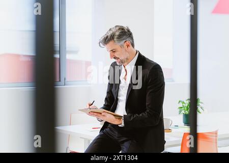 A focused executive in a sharp suit is busy at work, intently reviewing documents in a well-lit, contemporary office space Stock Photo
