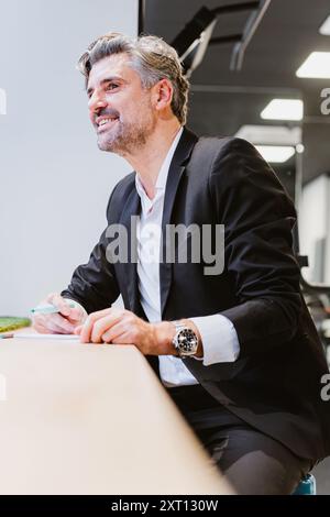 A dynamic executive leans on a conference table, engaging in a strategy session with a positive outlook in a modern office Stock Photo