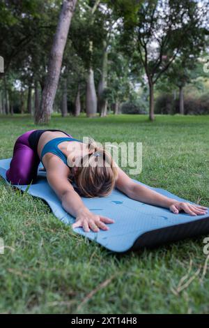 Unrecognizable young female in sportswear stretching while practicing yoga on mat on green grass in park in daylight Stock Photo