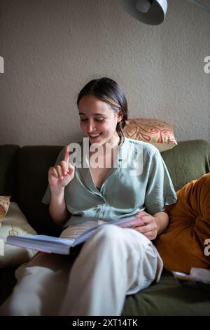Female sitting on sofa in living room and reading a book Stock Photo