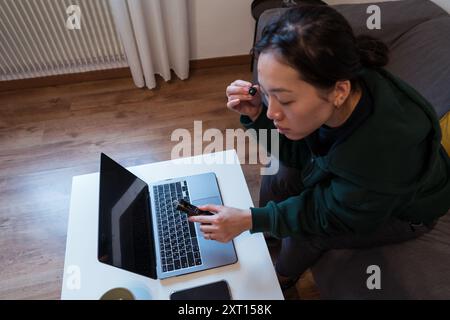 A focused woman uses a magnifying glass to closely examine the screen of a laptop, suggesting meticulous work or investigation Stock Photo