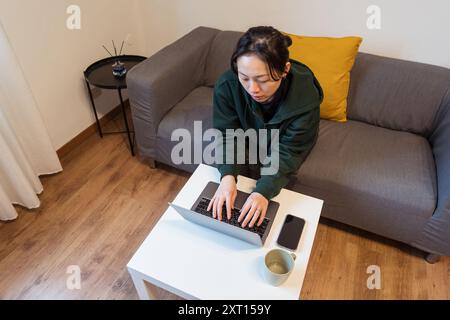 Woman works intently on a laptop at a modern minimalist home setting Stock Photo