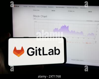 Person holding mobile phone with logo of American open-source software company GitLab Inc. in front of business web page. Focus on phone display. Stock Photo