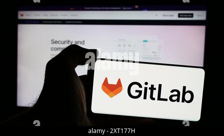 Person holding smartphone with logo of US open-source software company GitLab Inc. in front of website. Focus on phone display. Stock Photo