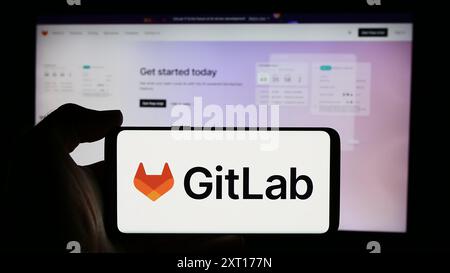 Person holding cellphone with logo of US open-source software company GitLab Inc. in front of business webpage. Focus on phone display. Stock Photo